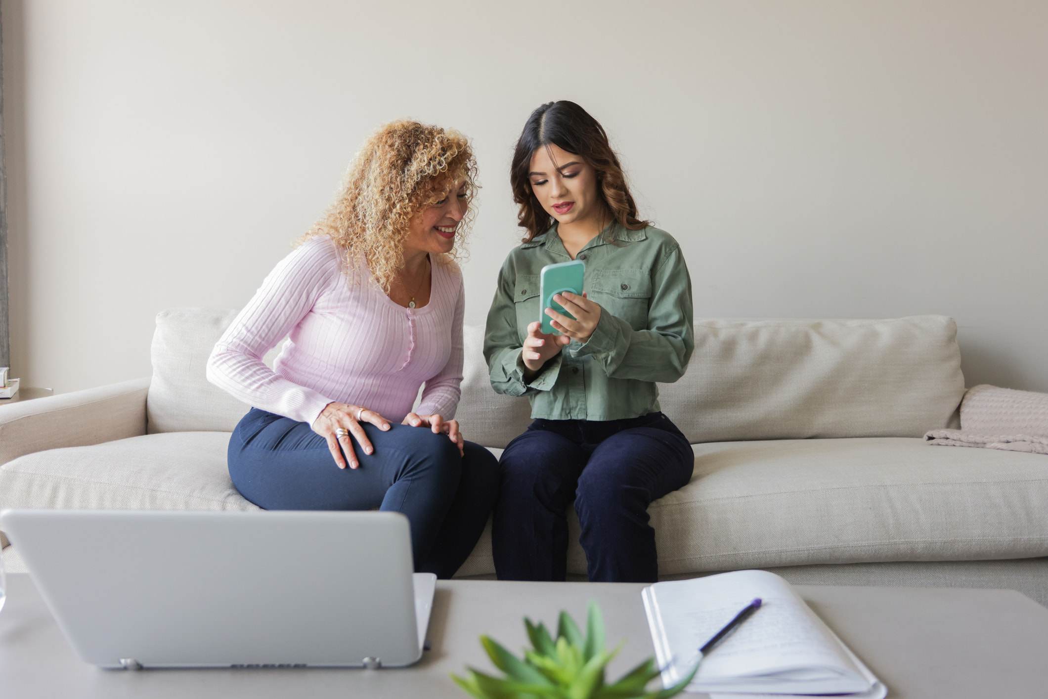 A mother and daughter sitting on couch reviewing financial information together on smartphone