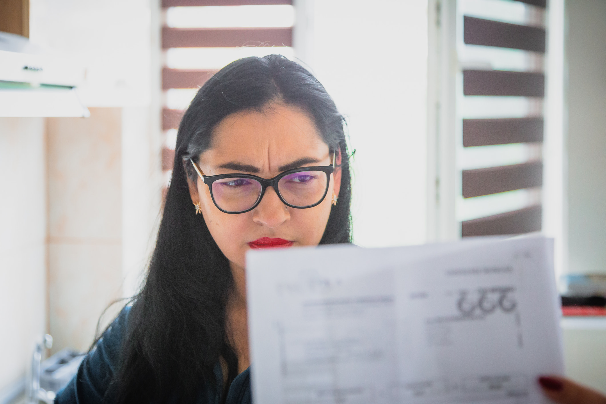 Woman wearing glasses carefully reading financial document at desk